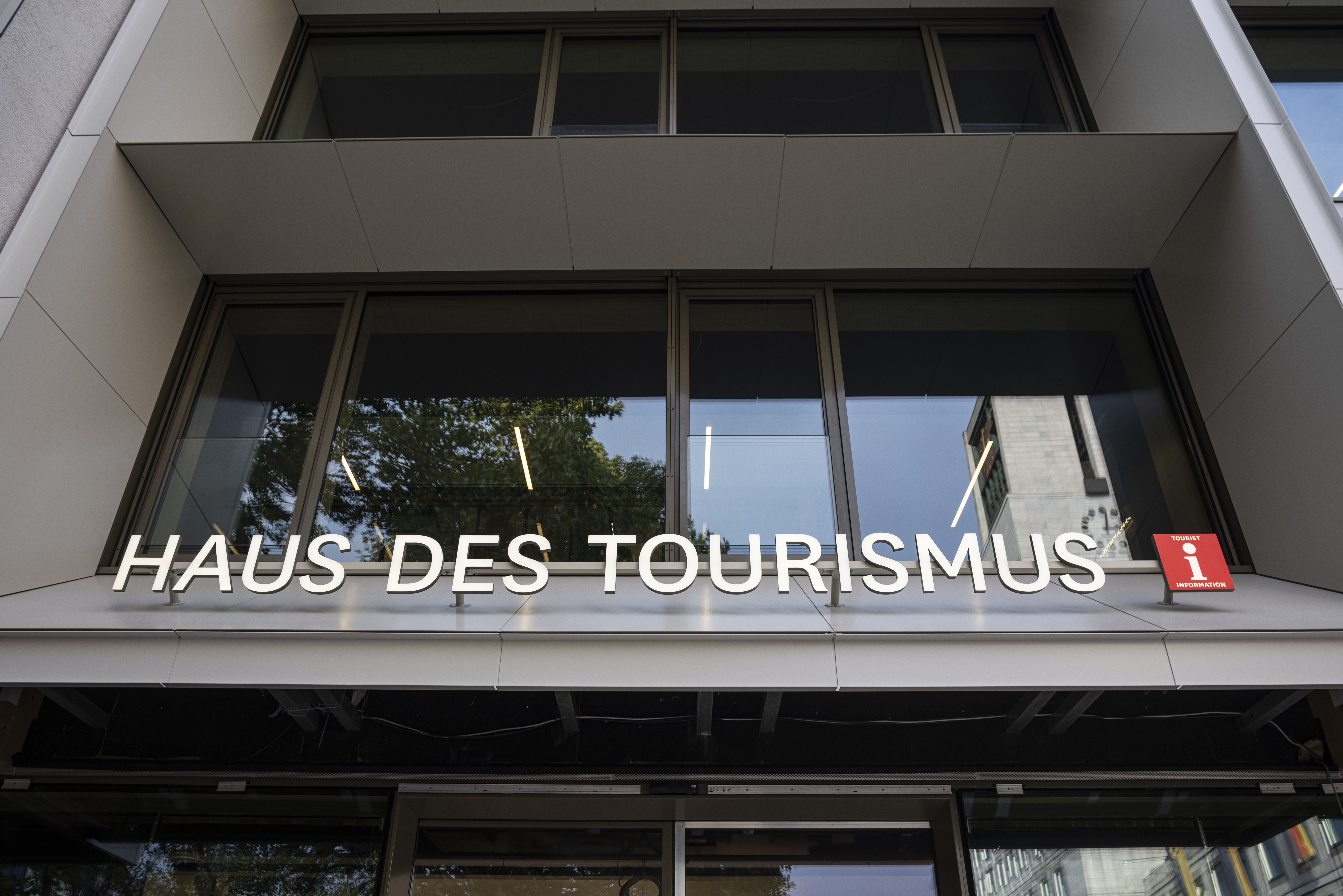 Eingang Tourist-Information, Stuttgart-Marketing GmbH, Sarah Schmid Weißer Schriftzug in Großbuchstaben über dem Eingang des i-Punkts. Dahinter das typische weiße "i" auf rotem Hintergrund, das die Tourist-Info symbolisiert.