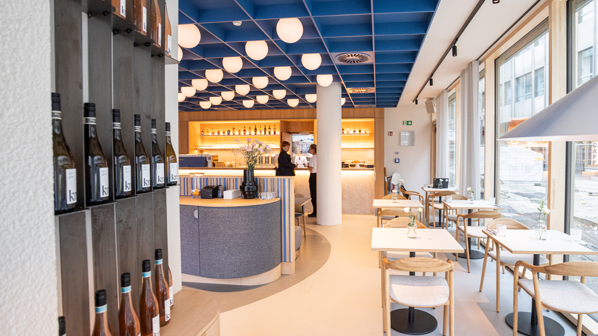 Gastraum knitz Restaurant,  Weinregal auf der linken Seite, geradeaus die Theke, rechts an den bodentiefen Fenstern kleine Tische mit je zwei Stühlen.